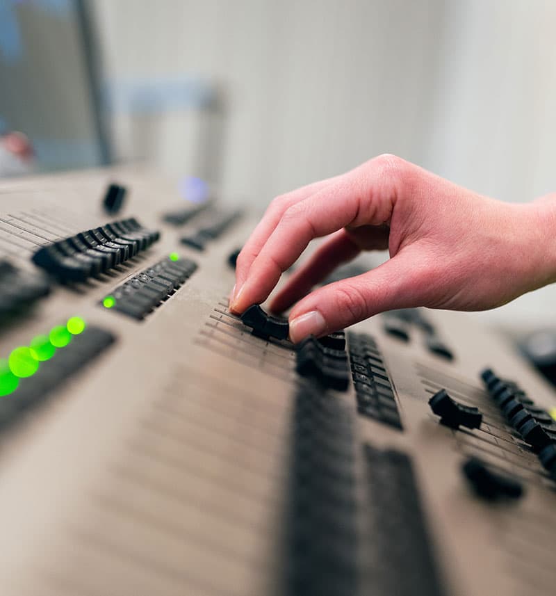 A hand adjusting a fader on an audio mixing console.