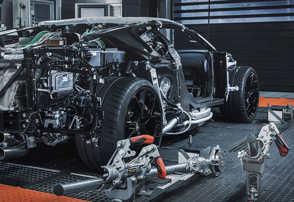 A sports car stripped to its carbon fibre tub, clamped on a test rig in a development bay.