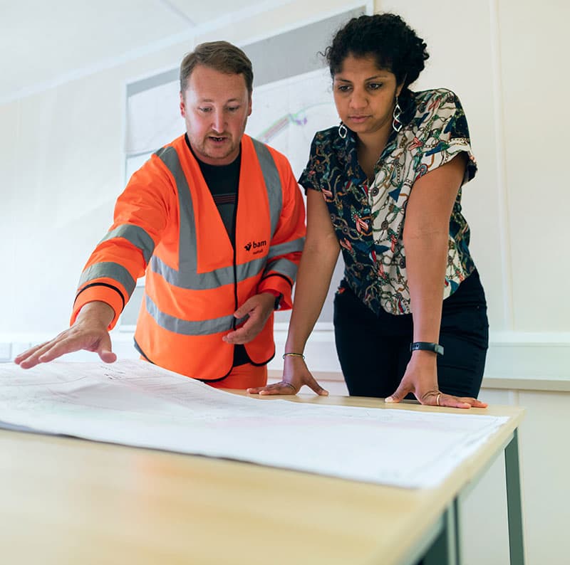 Two colleagues checking a part against a large technical drawing.