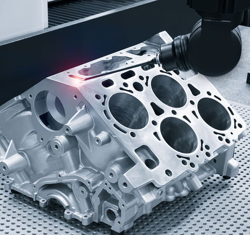 A laser scanner traces the deck face of a machined V6 engine block on a measuring table.