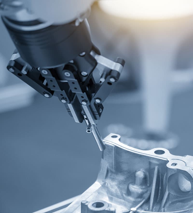 A robotic arm lowers a probe onto a cast aluminium housing on the inspection bench.