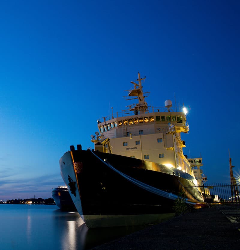 An ice-class vessel moored alongside a quay at dusk.